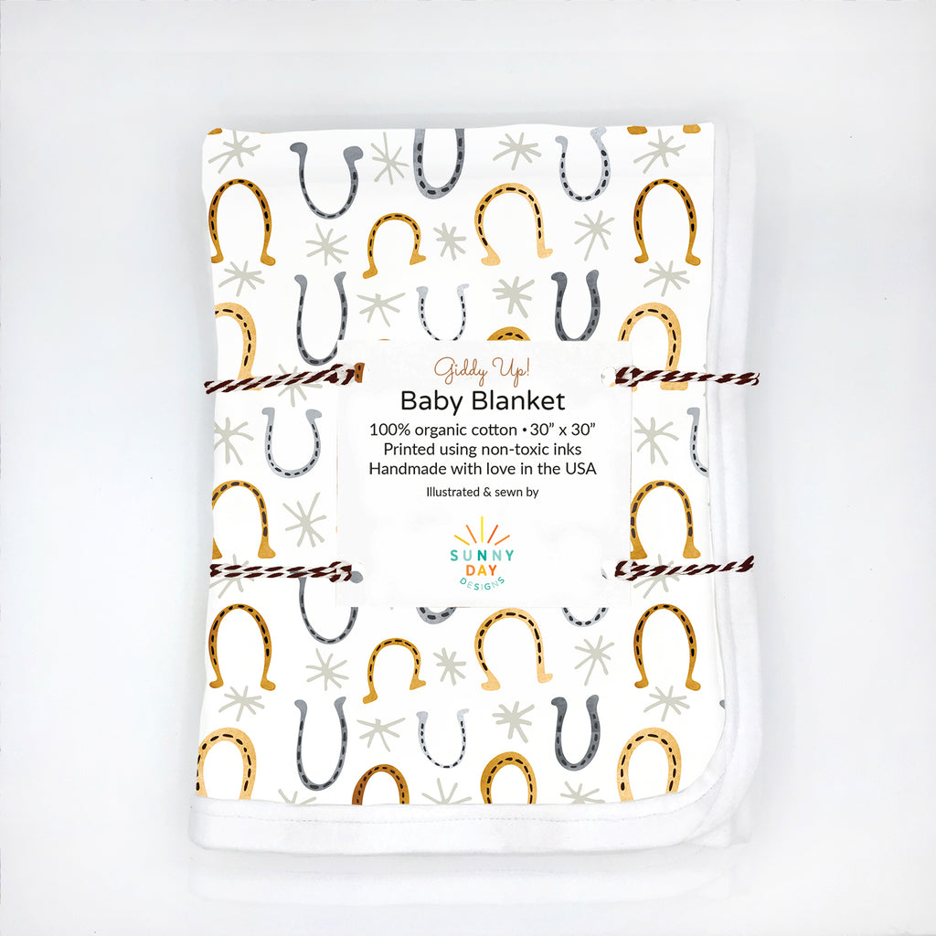 a packaged organic cotton baby blanket printed with a gray and golden watercolor horseshoe design