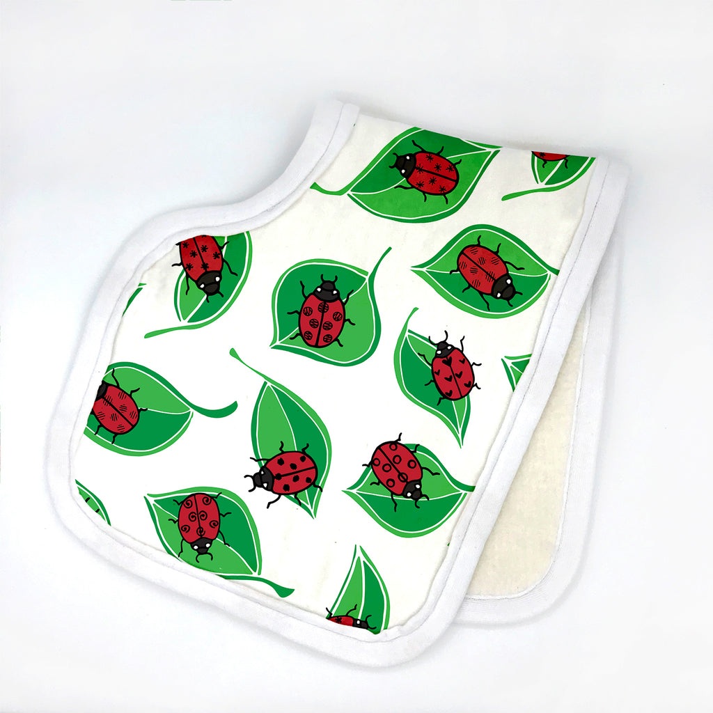 A printed baby burp cloth is folded in half and printed with red/black ladybugs on green leaves.