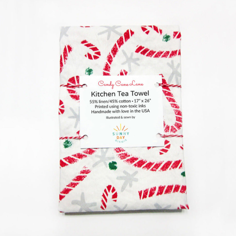Candy Cane Lane handmade linen/cotton red and white tea towel is folded and packaged on a white background. Made in the USA by Sunny Day Designs