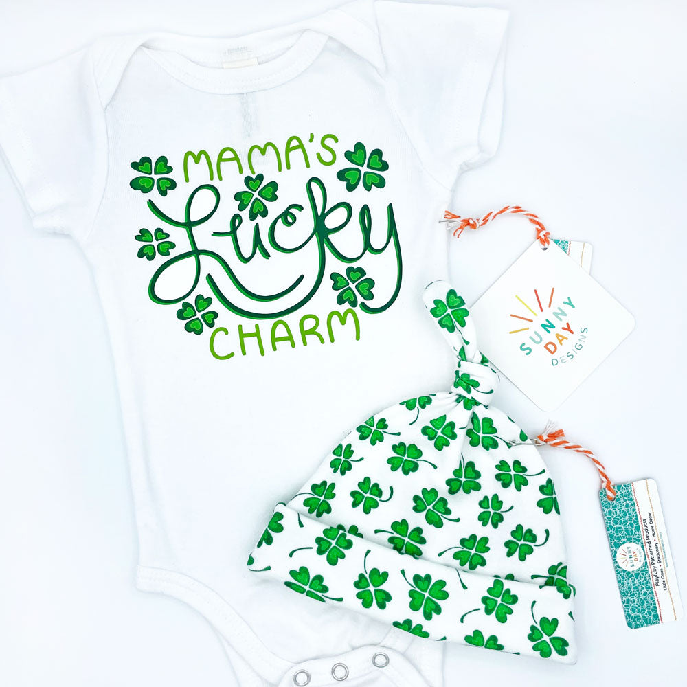 Green and white Mama's Lucky Charm St. Patrick's themed organic cotton baby onesie shown on a white background with coordinating Feeling Lucky organic cotton clover print newborn baby hat. Made in the USA by Sunny Day Designs.