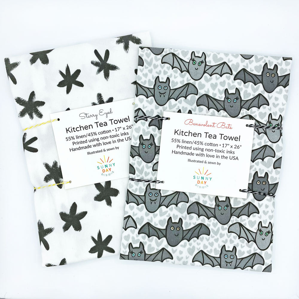 This set of 2 Halloween tea towels by Sunny Day Designs is more cute than spooky! Shown packaged and on a white background, this set of fun tea towels includes 1 black & white brushstroke star printed towel and 1 Benevolent Bats cheerful illustrated gray bat printed dish towel. Each is made in the USA.