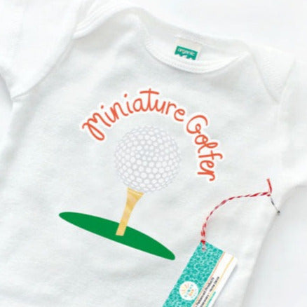 Close Up image of an organic cotton baby onesie printed with our Miniature Golfer artwork design. This punny artwork shows a golf ball on top of a golf tee with the workds "Miniature Golfer" above in orange hand lettered text.White, Gray, Green and Peach golf themed artwork design by Sunny Day Designs. Made in the USA.