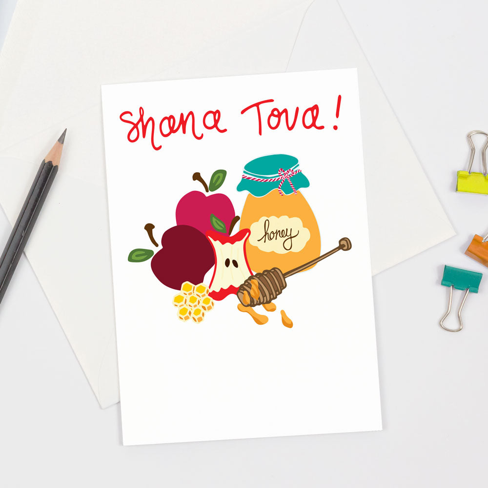 Shana Tova Rosh Hashanah Greeting Card by Sunny Day Designs. This fun greeting card is perfect for sending Jewish new year wishes and features 3 red apples, honeycomb, a jar of honey and a honey wand. The words "Shana Tova" also appear in red on the front of the card above the illustrated drawing. Made from sustainably sourced paper in the USA. Joyfully designed in Madison, WI.