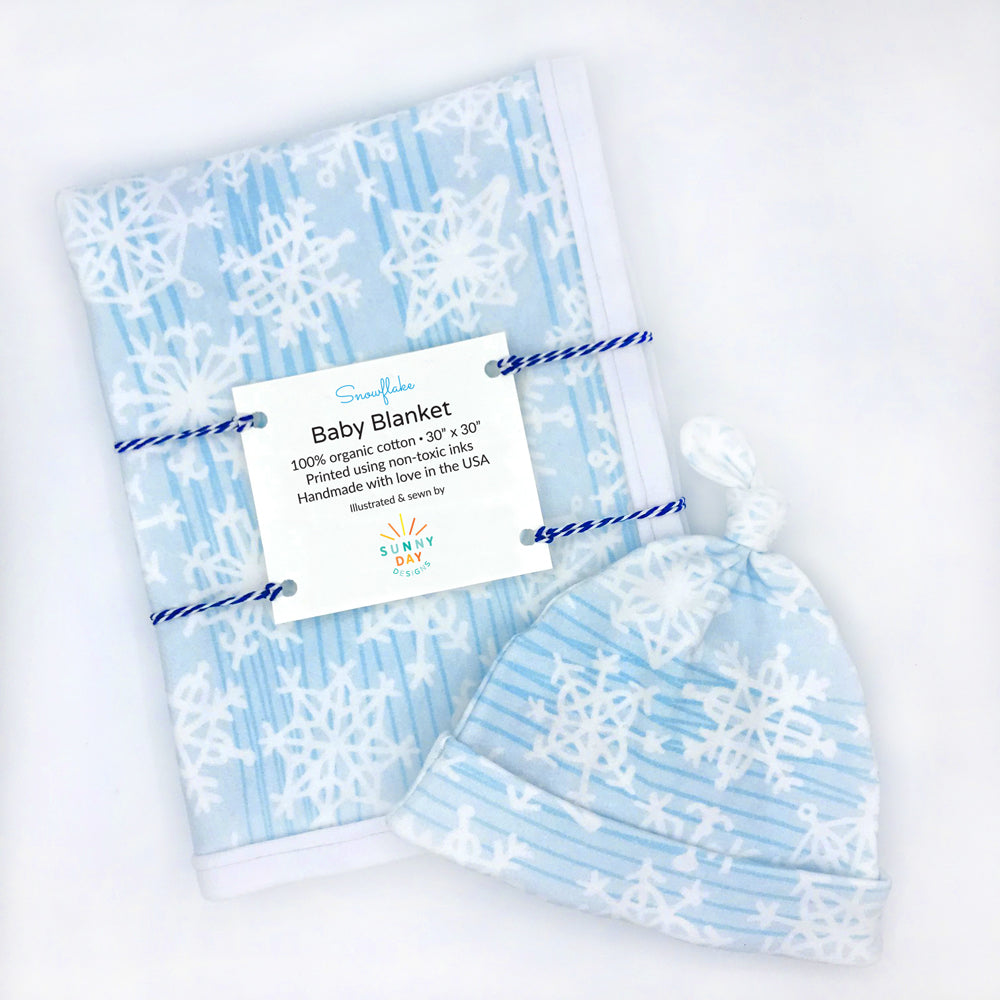 snowflake organic cotton baby gift set made in the USA by Sunny Day Designs with newborn hat and baby blanket in white snowflake print design with dark blue lines on light blue background 