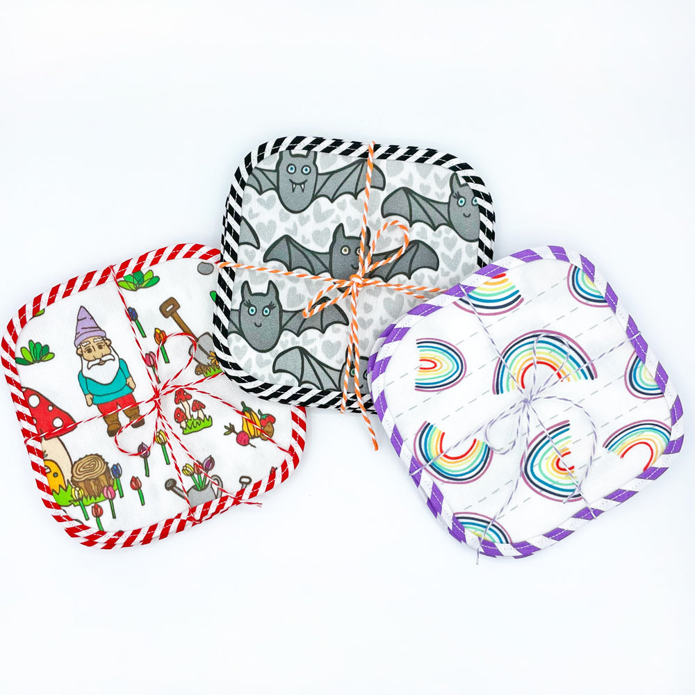 3 printed Fabric Cocktail Napkin sets by Sunny Day Designs. Each set of 4 cocktail napkins is tied with colorful baker's twine. Napkins are 5" square & printed with garden gnome, Halloween bats & Rainbow prints.