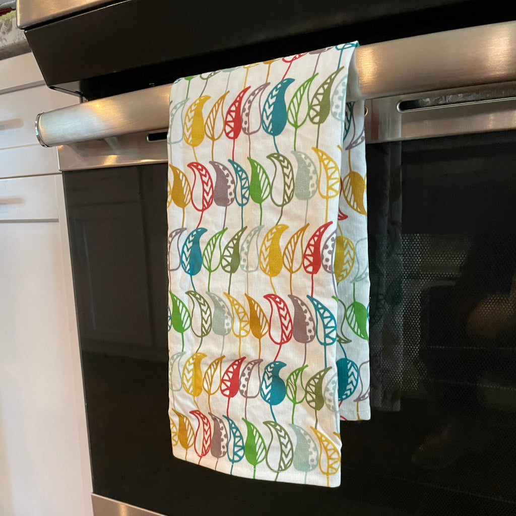 Colorful leaf printed Funky Foliage linen/cotton tea towel folded in half and hanging over oven door handle