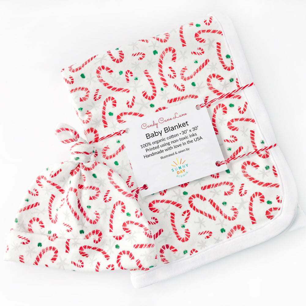 Colorful and cute red, gray, green, and white Candy Cane Lane printed organic cotton handmade baby blanket and newborn baby hat by Sunny Day Designs on a white background. A perfect baby gift set for Christmas or the holiday season!