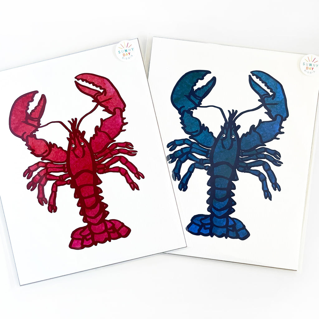 2 lobster-themed watercolor art prints by Sunny Day Designs are shown packaged and resting side-by-side on top of a white background. The wall art design on the left is a red lobster art print, while the art print design on the right is a wall art design of a rare blue lobster. These colorful coastal art prints make great gifts for anyone from Maine, New England or Massachusetts! Each nautical giclee wall art print is professionally printed & made in the USA. Designed by Sunny Day Deisgns in Madison, WI.