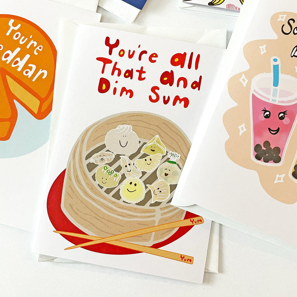 3 Greeting Cards designed by Sunny Day Designs are shown Close Up, including 1 featuring a variety of smiling steamed dim sum dumplings, a bamboo steamer basket, and chopsticks with text that says: You're All That And Dim Sum".