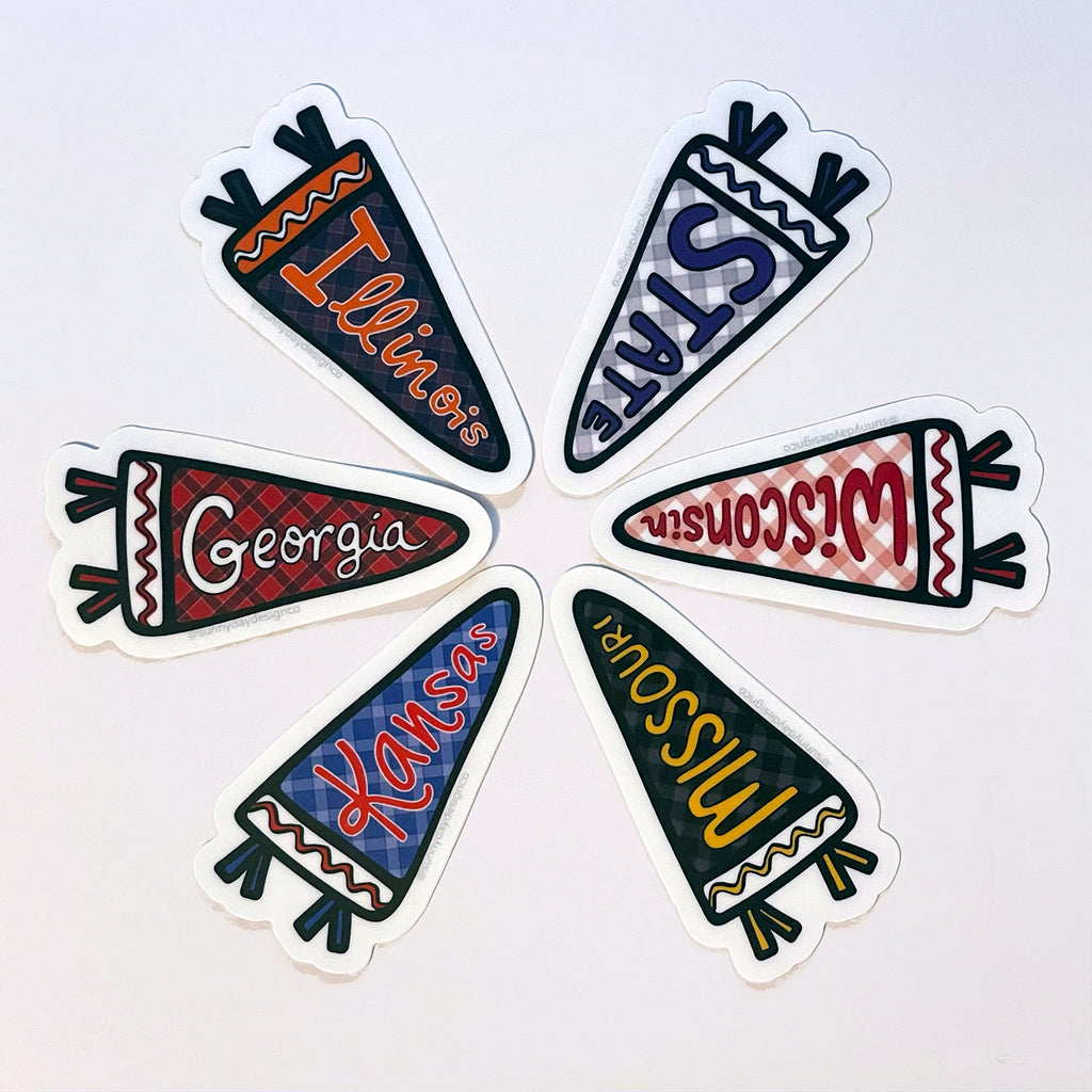 6 sports pennant-shaped college & university-themed laptop stickers are fanned out in a circular shape on a white background. The stickers shown include the navy/orange Illinois Pennant Vinyl Sticker, the purple/gray/white State Pennant Kansas Vinyl Sticker, the red/white Wisconsin Pennant Vinyl Sticker, the black/golden yellow Missouri Pennant Vinyl Sticker, the blue/red/white/Kansas Pennant Vinyl Sticker & the red/black/white Georgia Pennant Vinyl Sticker. Designed by Sunny Day Designs & made in the USA.