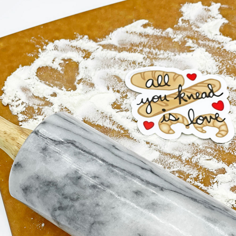 Marble rolling pin on a wooden surface with flour and a decorative vinyl sticker by Sunny Day Designs featuring a pun of the quote "All You Knead Is Love" that bakers will love!