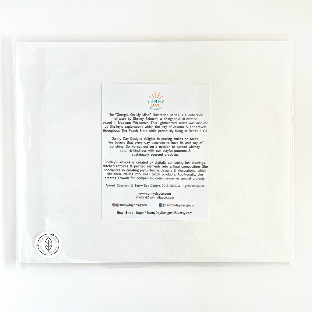 Back view of the 'Georgia On My Mind' art print by Sunny Day Designs, featuring an artist information sheet that shares inspiration and details about the artwork and creator Shelley Schmidt. The print is packaged in a clear sleeve with branding and a sustainability sticker at the bottom left.