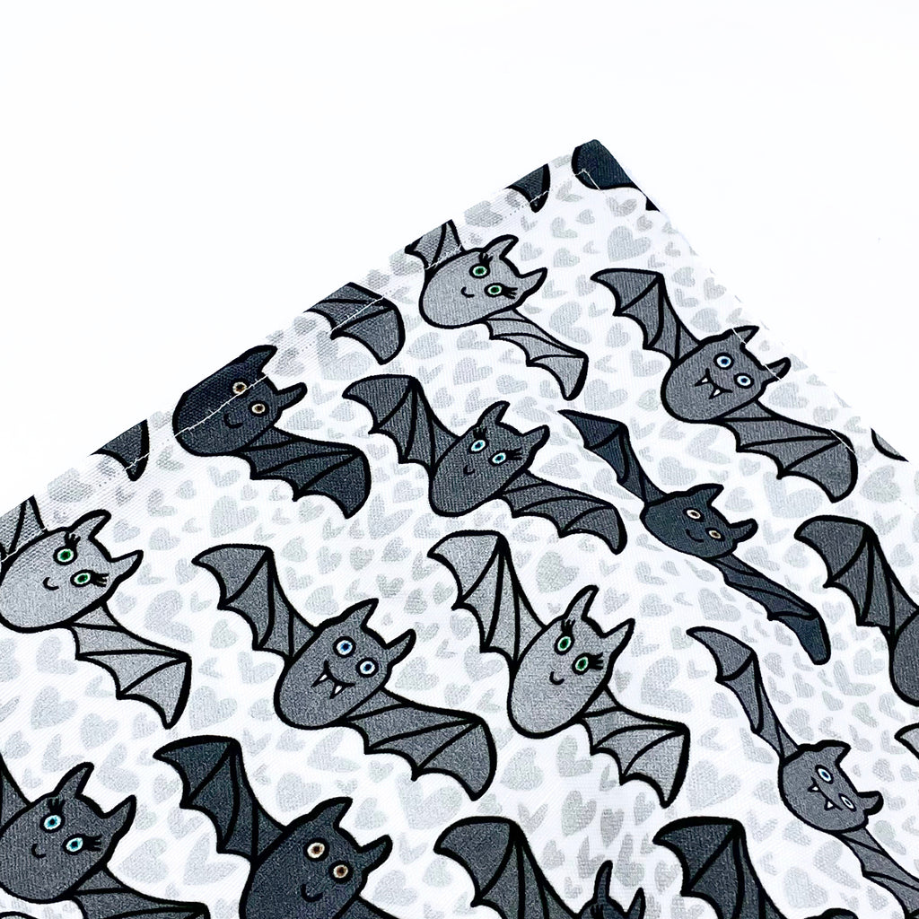 A close up of the corner of a gray, linen/cotton fabric printed bat-themed Halloween kitchen tea towel by Sunny Day Designs. The perfect tea towel to use in your kitchen during October!