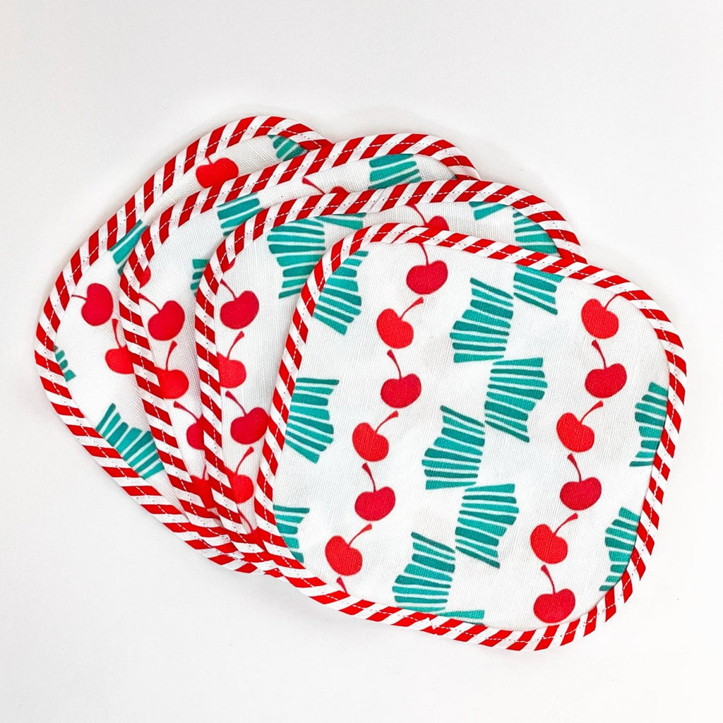 Fanned-out set of four Cheerful Cherries fabric cocktail napkins. The napkins feature vibrant red cherry patterns and teal striped bows on a white background, edged with red and white striped trim, perfect for adding a fun touch to any table setting.