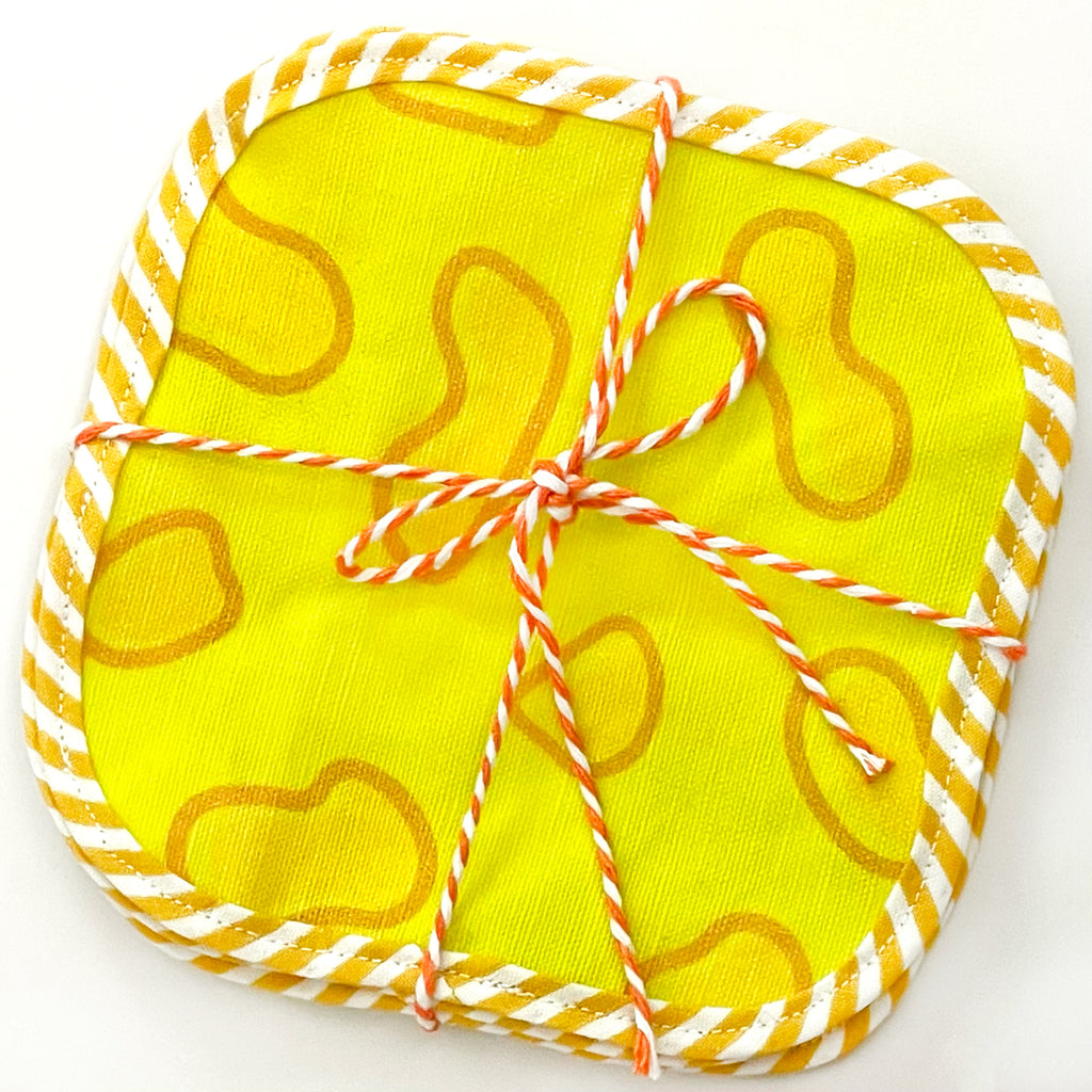 Packaged set of yellow cheese-themed fabric cocktail napkins tied neatly with orange and white twine. The napkins feature a bright yellow background with fun cheese shapes, making them a playful addition to any gathering.