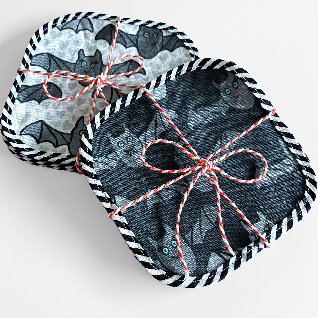 This reusable fabric set of 8 Halloween cocktail napkins features 4 light gray bat printed napkins and 4 dark gray bat printed napkins and both sets of 4 napkins are shown packaged with orange/white baker's twine on a white background. Handmade in the USA by Sunny Day Designs, these eco-friendly Halloween party napkins are perfect for Halloween lovers or as a Halloween host gift!