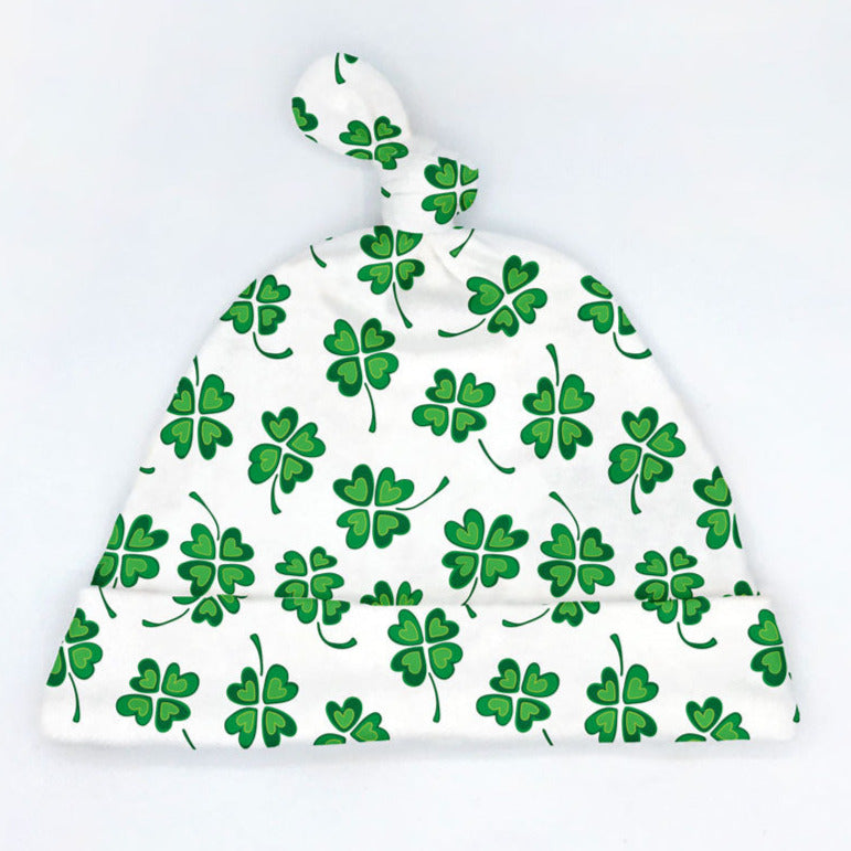 A green and white four-leaf clover printed newborn baby hat with a tie-top design is shown on a white background