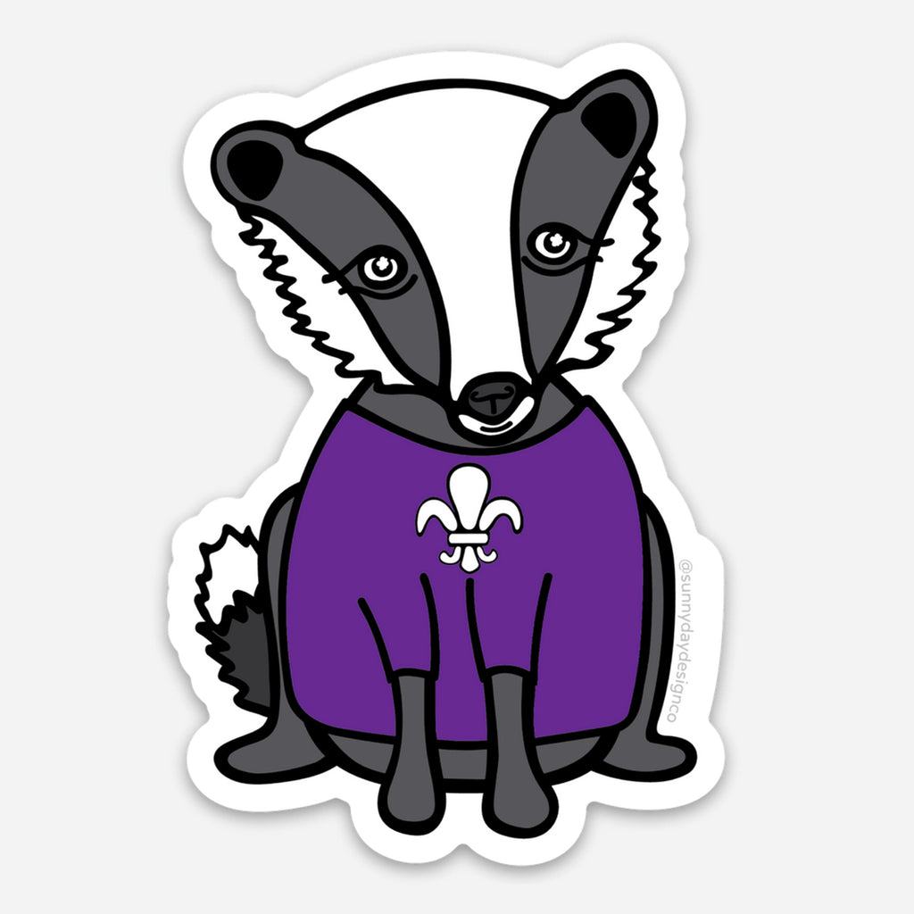 An animal-themed vinyl sticker of a cute gray/white badger wearing a purple shirt with a white fleur de lis symbol on the front, the symbol of Spring Hill College