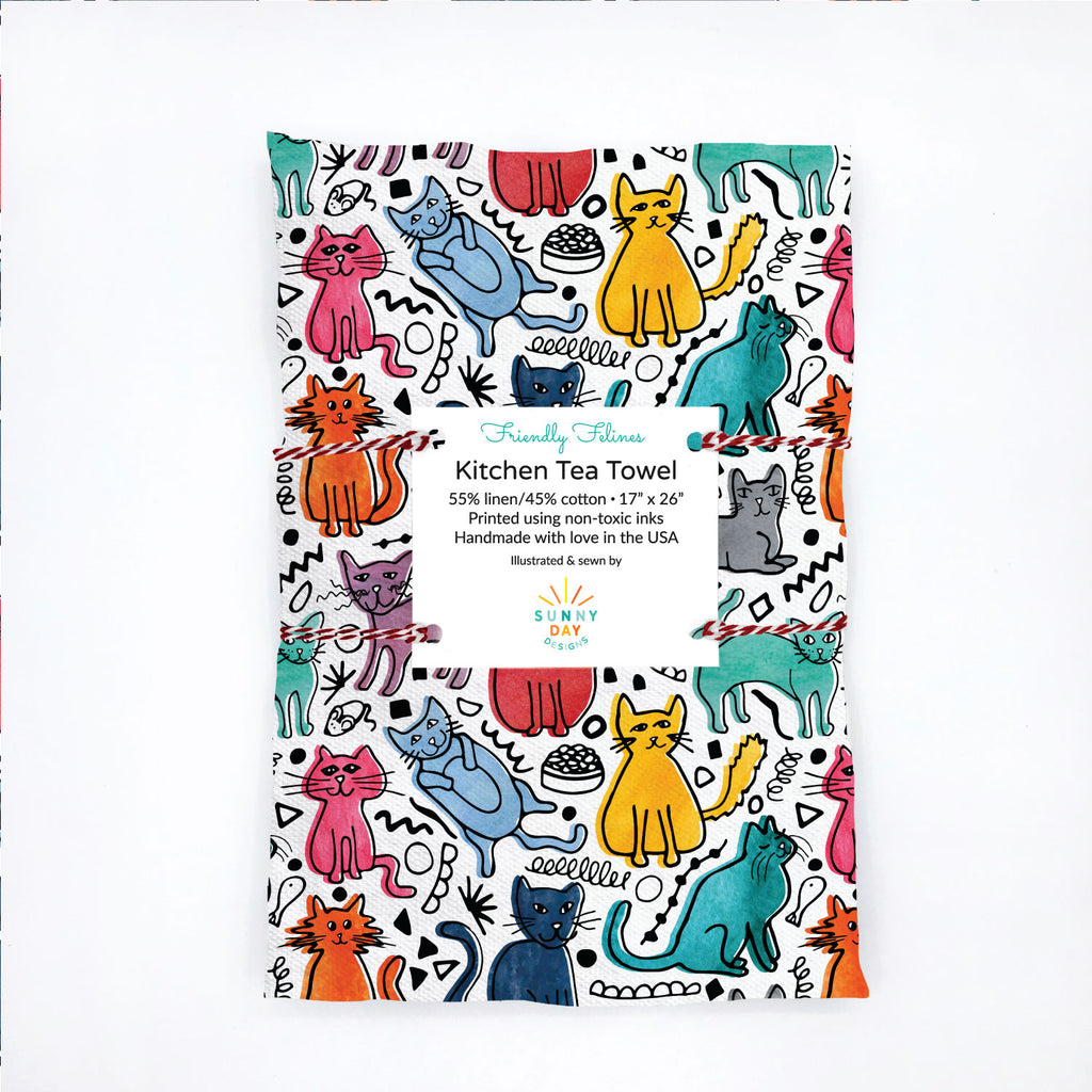 A cat-themed packaged tea towel featuring friendly felines in brightly colored watercolor shades with black scribble accents.