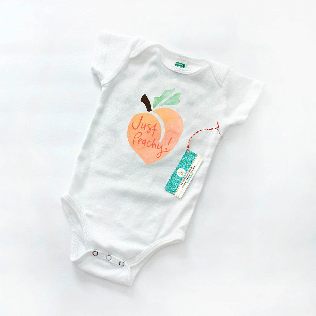 An adorable peach-themed organic cotton baby onesie is shown on a white background - this cute design features an orange, green, and brown watercolor peach fruit with hand lettered "Just Peachy!" text. This cute & colorful baby bodysuit is inspired by the Southern saying "Just Peachy!", making it a perfect southern baby shower gift or a unique Georgia baby gift. Made in the USA and designed by Sunny Day Designs in Madison, WI.