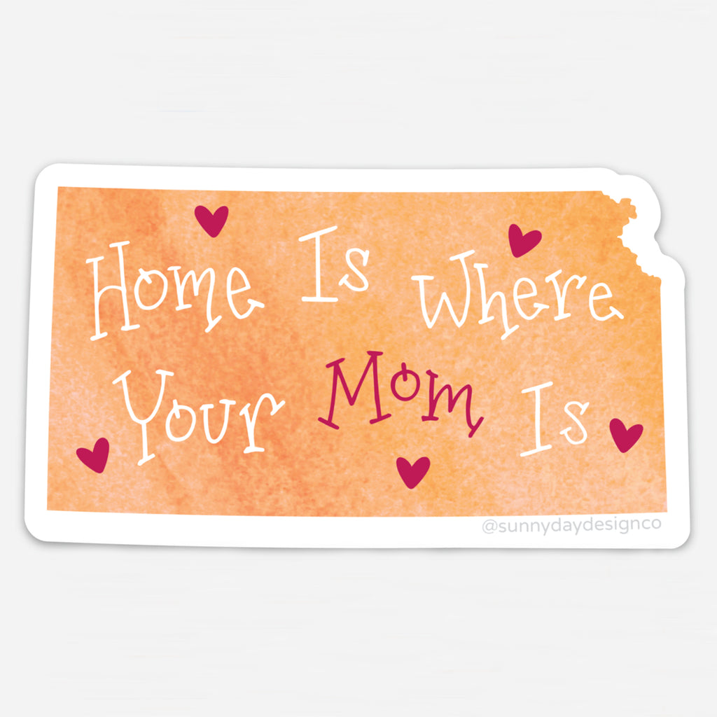 Vinyl magnet shaped like the state of Kansas with a soft orange watercolor background and the phrase “Home Is Where Your Mom Is” in white and magenta whimsical lettering, accented with magenta hearts. Die-cut with a white border, designed by Sunny Day Designs.