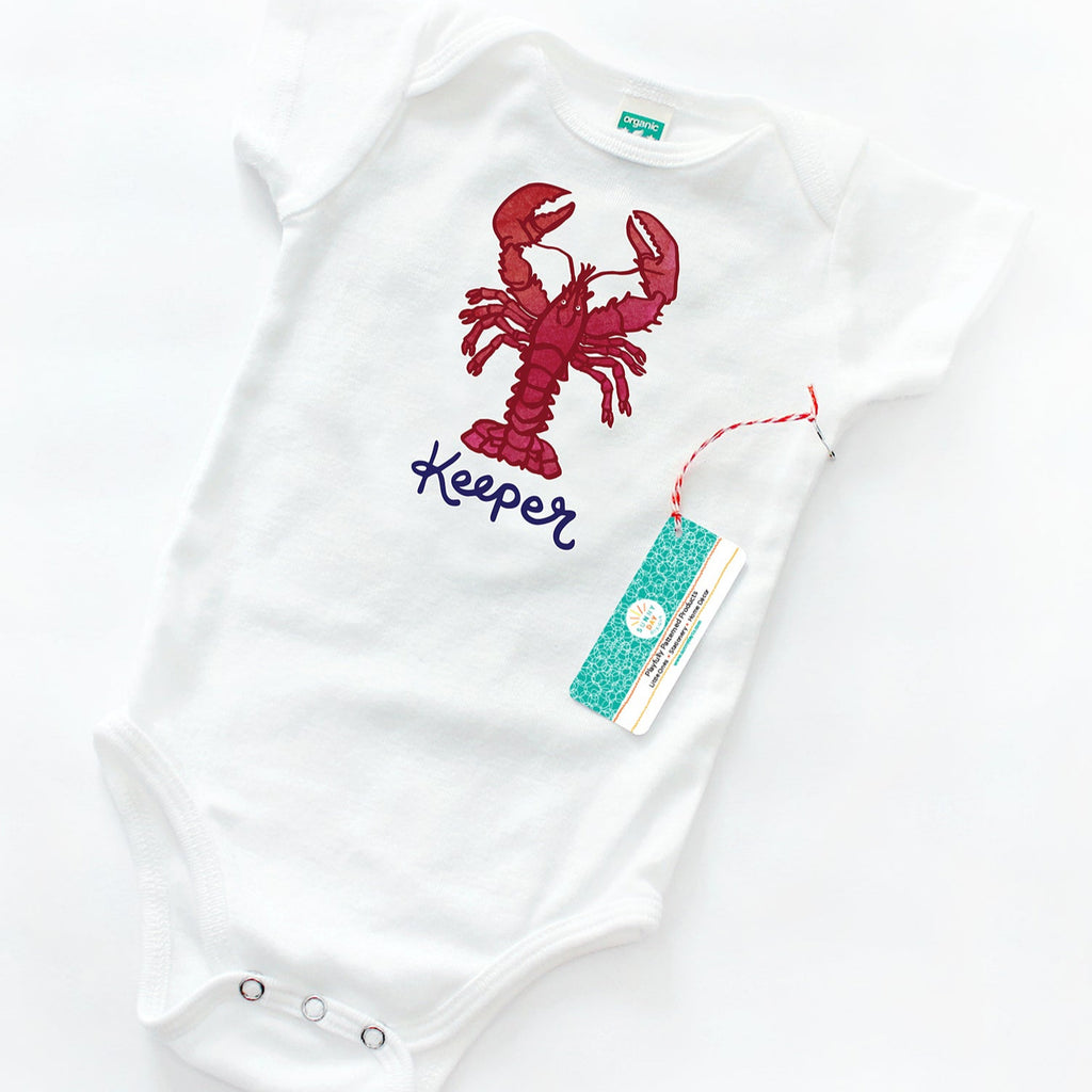 White baby onesie featuring a bright red illustrated lobster with the word “Keeper” in deep blue script font. Flat lay presentation on a white background with eco-friendly Sunny Day Designs branding tag.