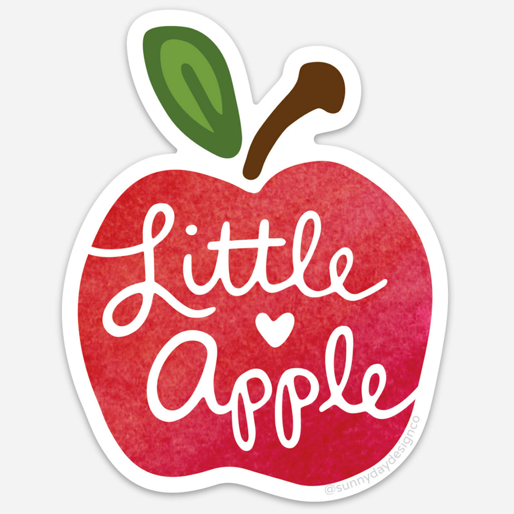 Vinyl magnet shaped like a bright red apple with a green leaf and brown stem, featuring the phrase “Little Apple” in playful white script with a heart accent. Die-cut with a white border, celebrating Manhattan, Kansas, by Sunny Day Designs.
