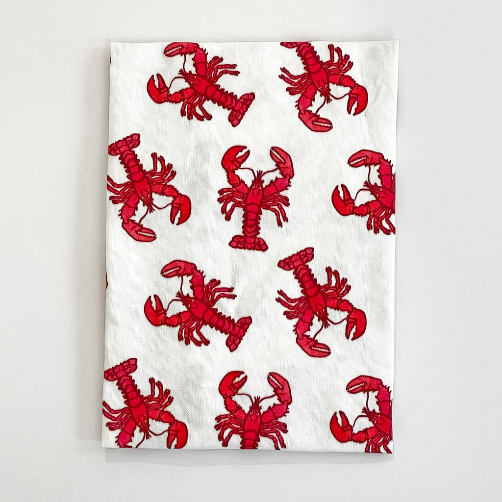 Lobster Tea Towel laid out with multiple red lobster illustrations on a white fabric. The towel is ideal for adding a playful and coastal vibe to any kitchen or dining space.