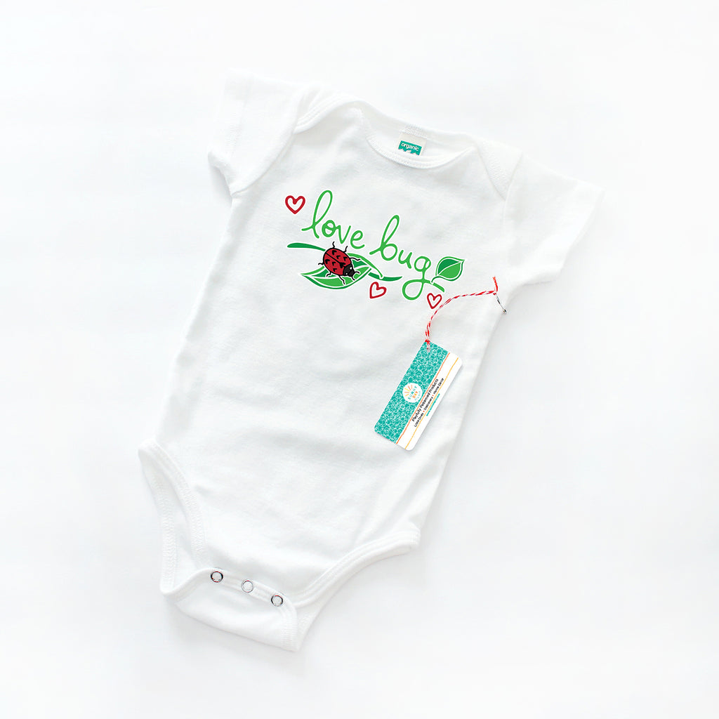 White organic cotton baby onesie printed with a green, red, and black ladybug and leaf print design with green text that says "Love Bug" by Sunny Day Designs.