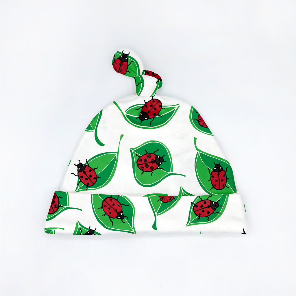 A red, black, and green Ladybug printed organic cotton baby hat with tie top.