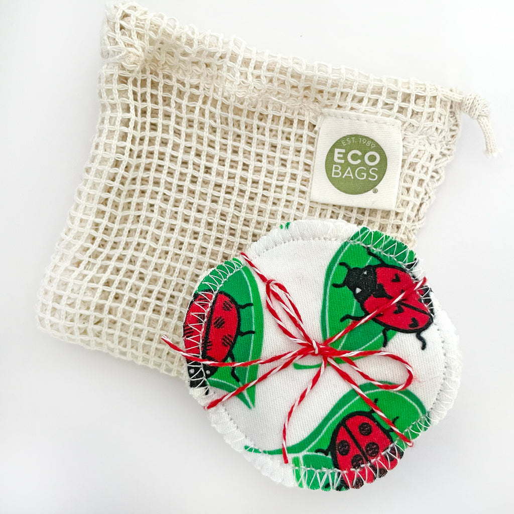Packaged reusable facial rounds with vibrant red, black & white
ladybug  on green leaf design, placed beside an eco-friendly wash bag.
