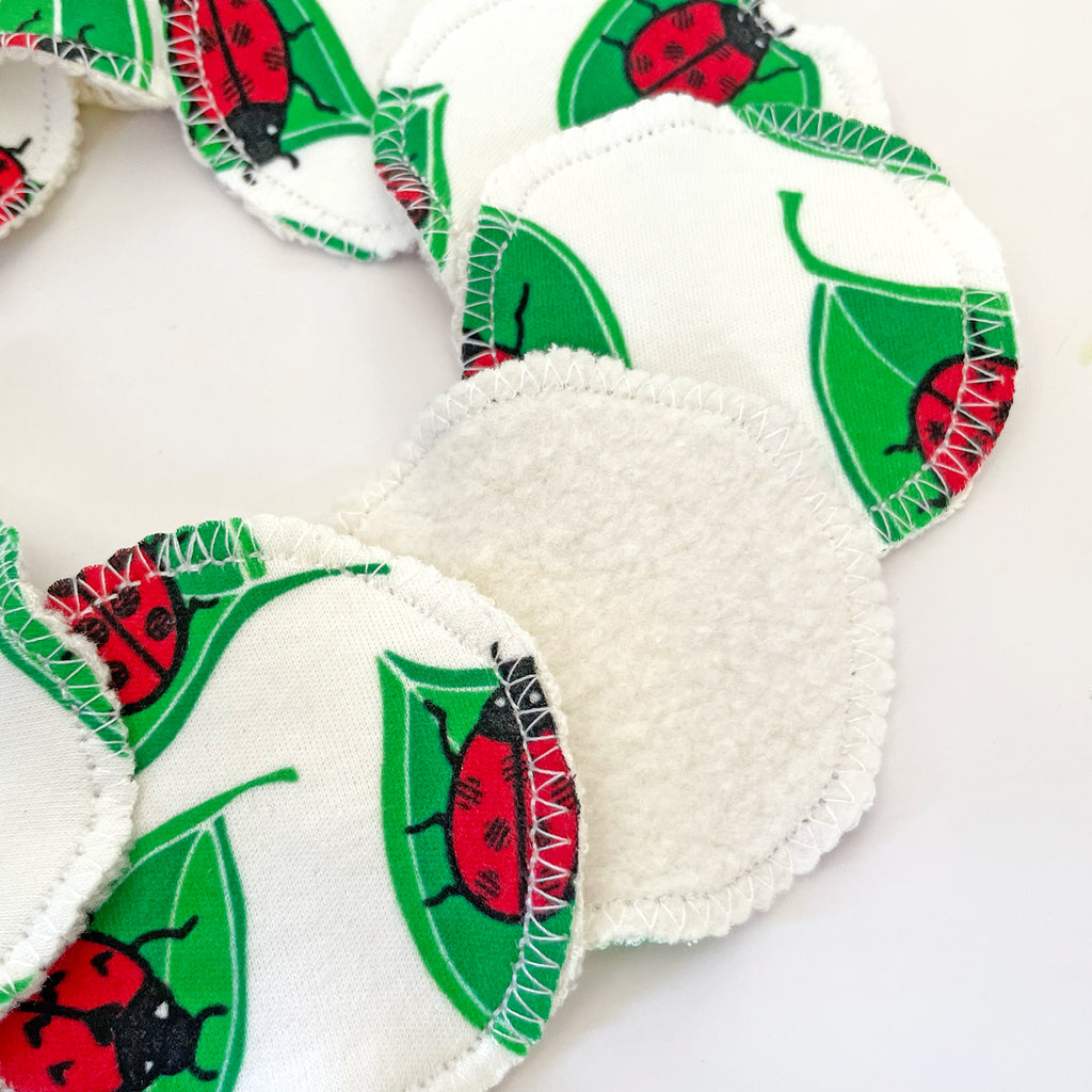 Reusable facial rounds fanned out in a circular arrangement with a close-up of one showing the soft fleece backing, featuring a ladybug pattern on each wipe.