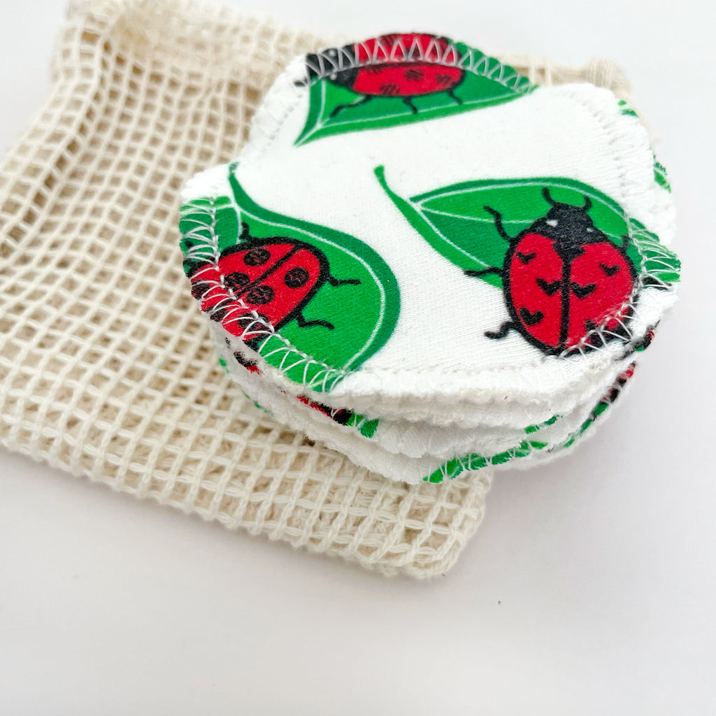 Stack of reusable facial rounds with a cute ladybug pattern, resting on an eco-friendly mesh wash bag.