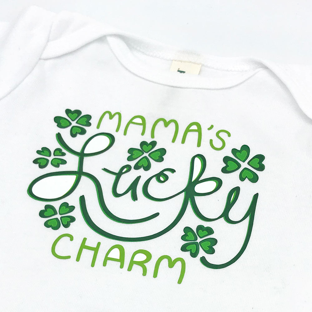 A close up image of one of our Feeling Lucky printed baby onesie designs is shown for a better view of the green and white Irish themed shamrock design that is perfect for St. Patrick's Day and features the words "Mama's Lucky Charm" with 6 green shamrock motifs