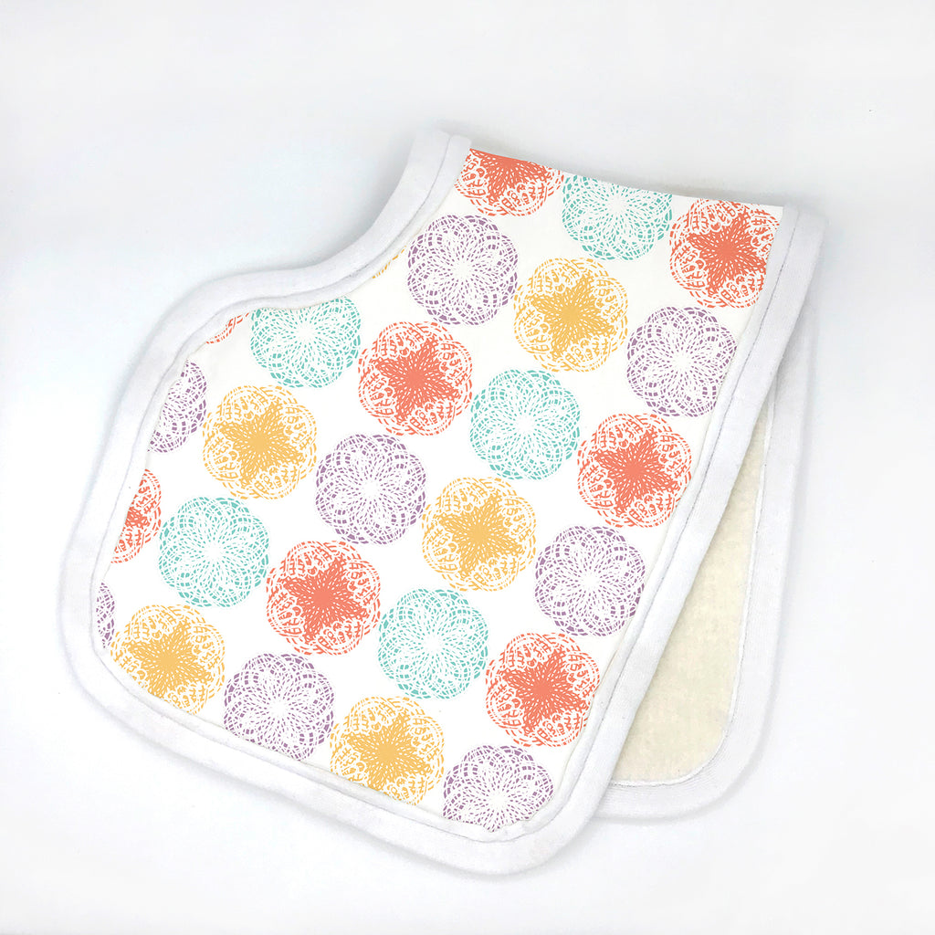 Contoured white baby burp cloth featuring a repeating mandala-style floral pattern in pastel tones of orange, mint, lavender, and yellow. Displayed folded in half with white edging on a clean white background, part of the Modern Mandala eco-friendly line by Sunny Day Designs.