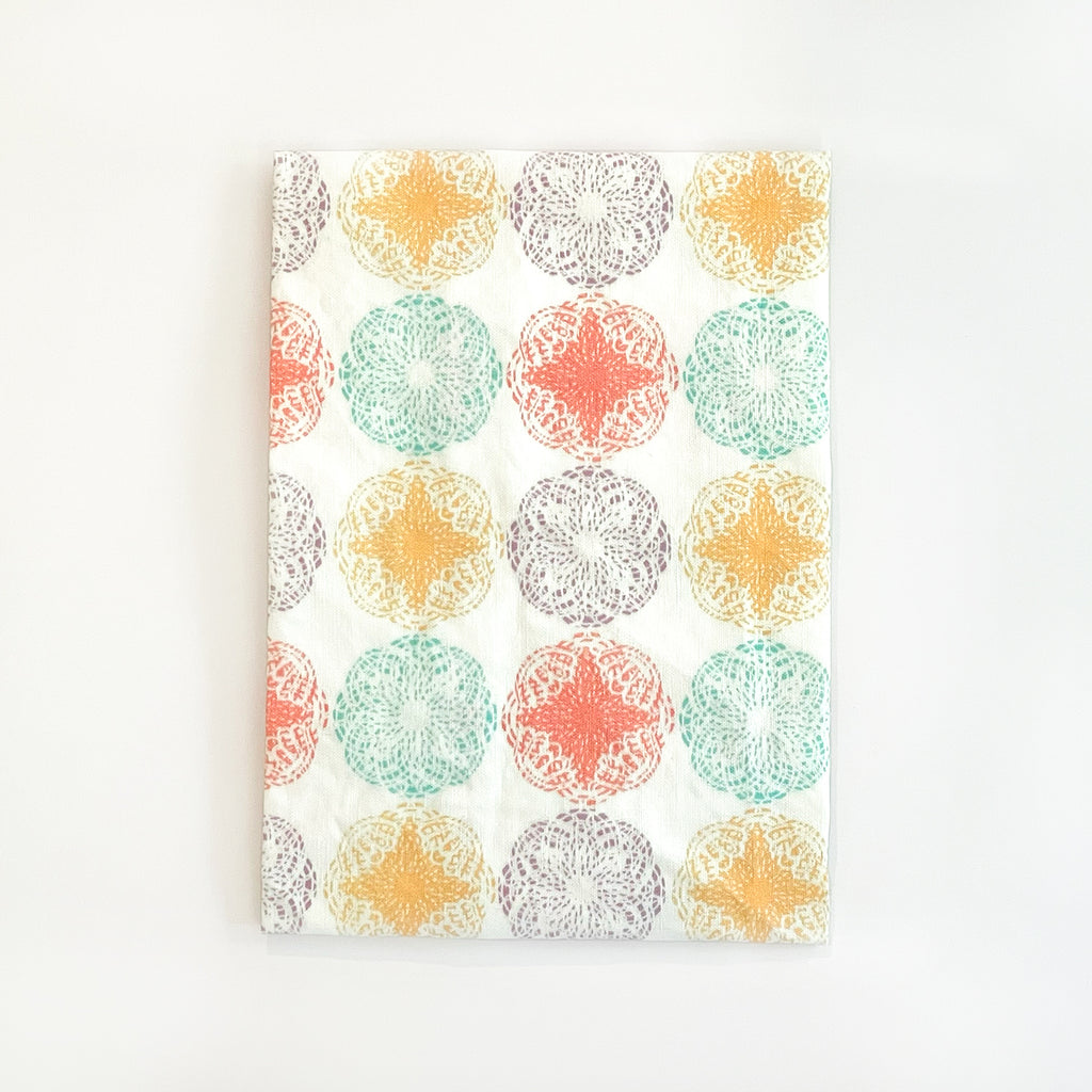 Tea Towel with a repeated pattern of colorful mandalas in yellow, orange, teal, and purple on a clean white fabric. The towel’s unique and modern print makes it both functional and decorative for kitchen use.