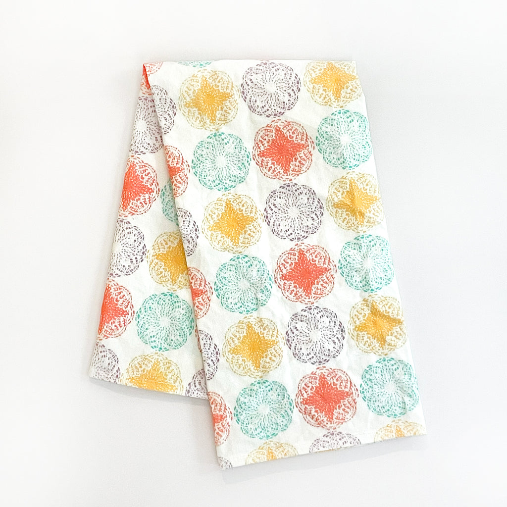 Modern Mandala Tea Towel folded neatly, displaying its vibrant circular mandala designs. The towel features bright colors like yellow, teal, orange, and purple on a white background, perfect for adding a splash of color and style to any kitchen setting.