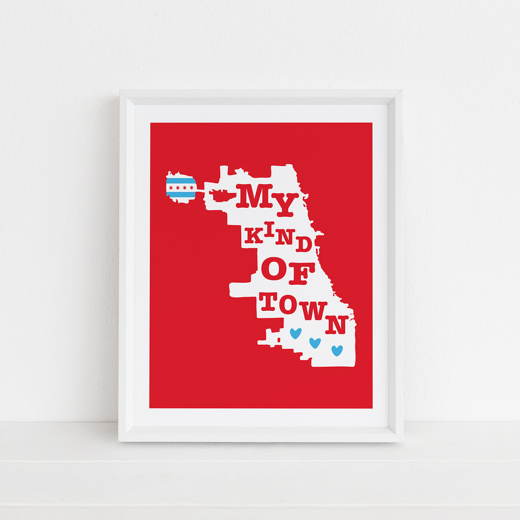 A red, white & blue Chicago themed wall art print (8x10 size) featuring the city limit map outline of the city of Chicago, Illinois, with the words "My Kind Of Town" in hand lettered script and the Chicago flag motif is shown inside a white picture frame. This print features the colors of the Chicago flag: red, white, and blue.