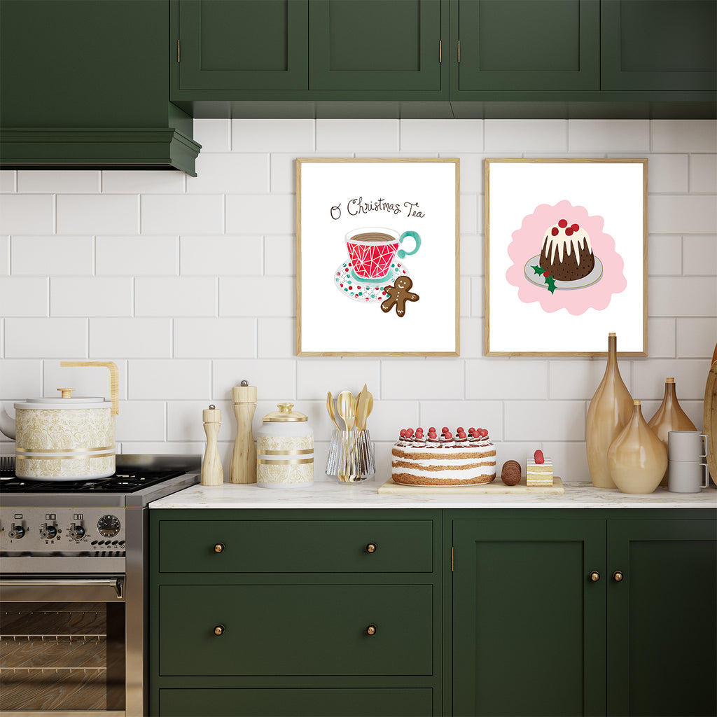 A beautiful and tastefully decorated kitchen with forest green cabinets and a white subway tile backsplash featuring 2 framed 8x10 sized art prints is shown with a beautifully decorated cake and other desserts on the countertop, alongside several decorative canisters, containers and utensils. Inside the 2 picture frames that are hung up on the backsplash are the O Christmas Tea holiday food pun art print and the Christmas Pudding holiday dessert art print, both are made in the USA by Sunny Day Designs.