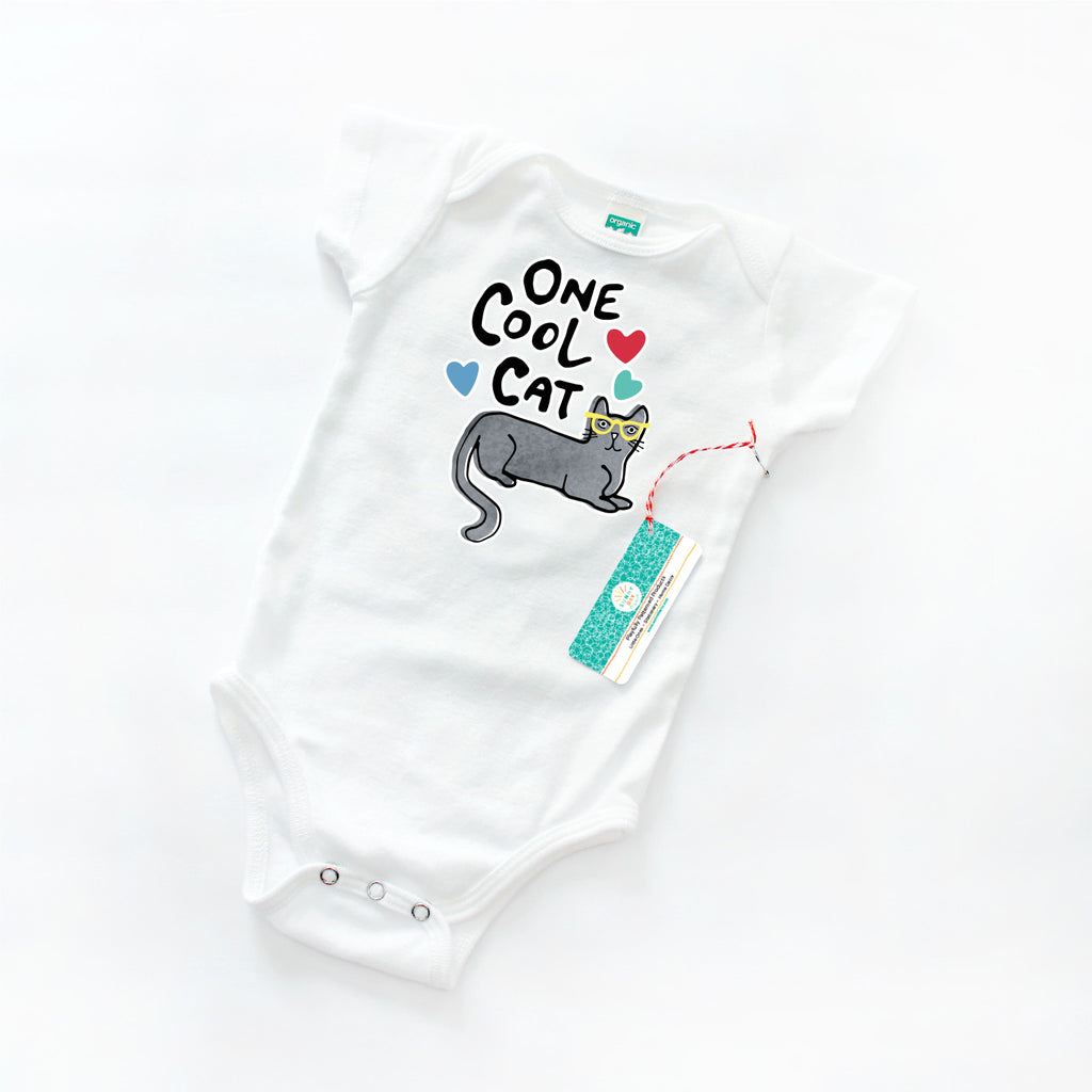 A cat-themed baby onesie is printed with a gray cat wearing yellow sunglasses, 3 colorful hearts, and black "One Cool Cat" text. Shown on a white background.