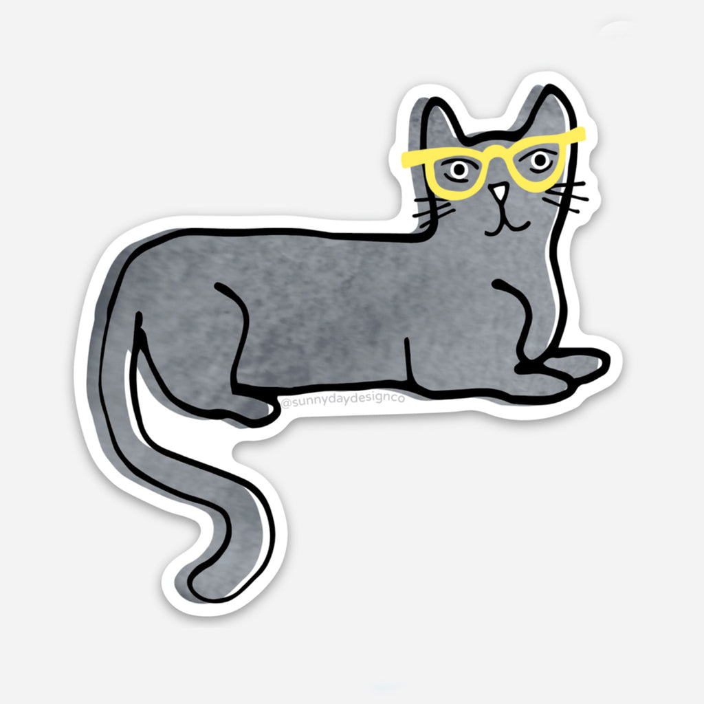 An adorable die cut vinyl sticker design featuring an illustrated gray watercolor cat wearing yellow sunglasses. The cat is laying down on it's belly with it's tail curled downward.