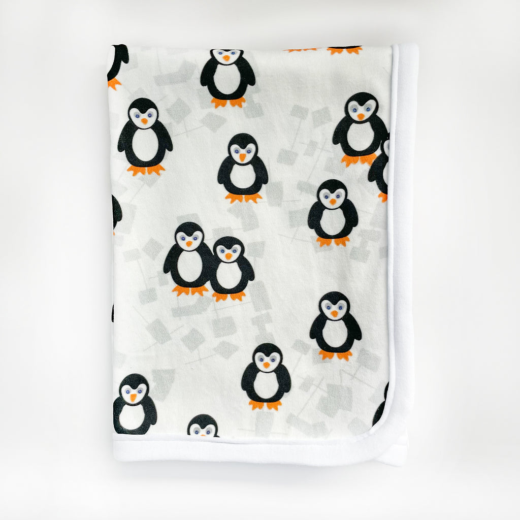 An adorable white, black, and orange penguin printed baby blanket by Sunny Day Designs is shown folded and un-packaged on a white background.