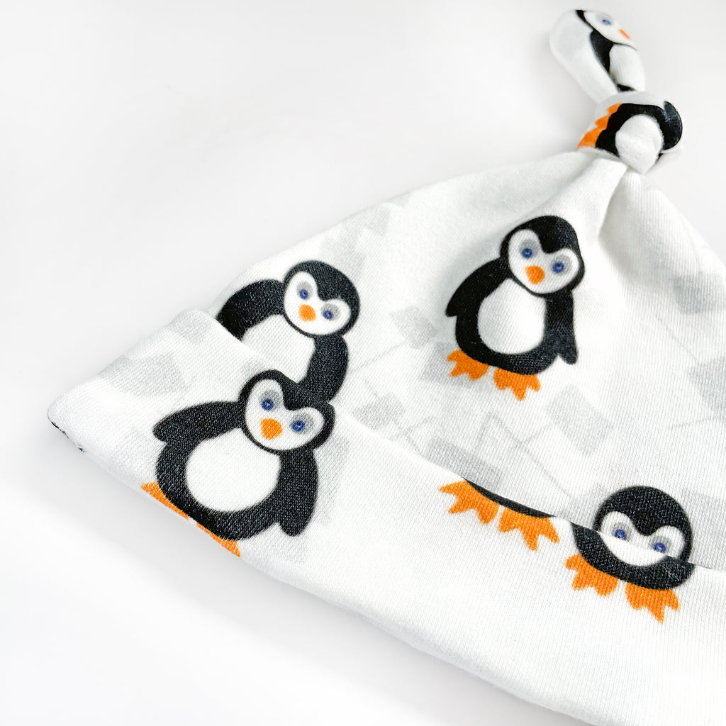 A close up view of an adorable black, white, blue and orange organic cotton baby hat made from penguin print fabric by Sunny Day Designs