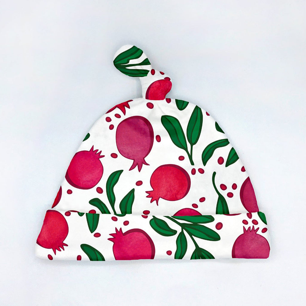 A colorful gender neutral pomegranate printed newborn baby hat by Sunny Day Designs is shown with an adjustable tie top knot feature that fits babies 0-3 months. This cute pomegranate fruit printed baby gift is proudly made in the USA and makes a fun baby shower gift for Jewish babies, foodie parents-to-be and more!