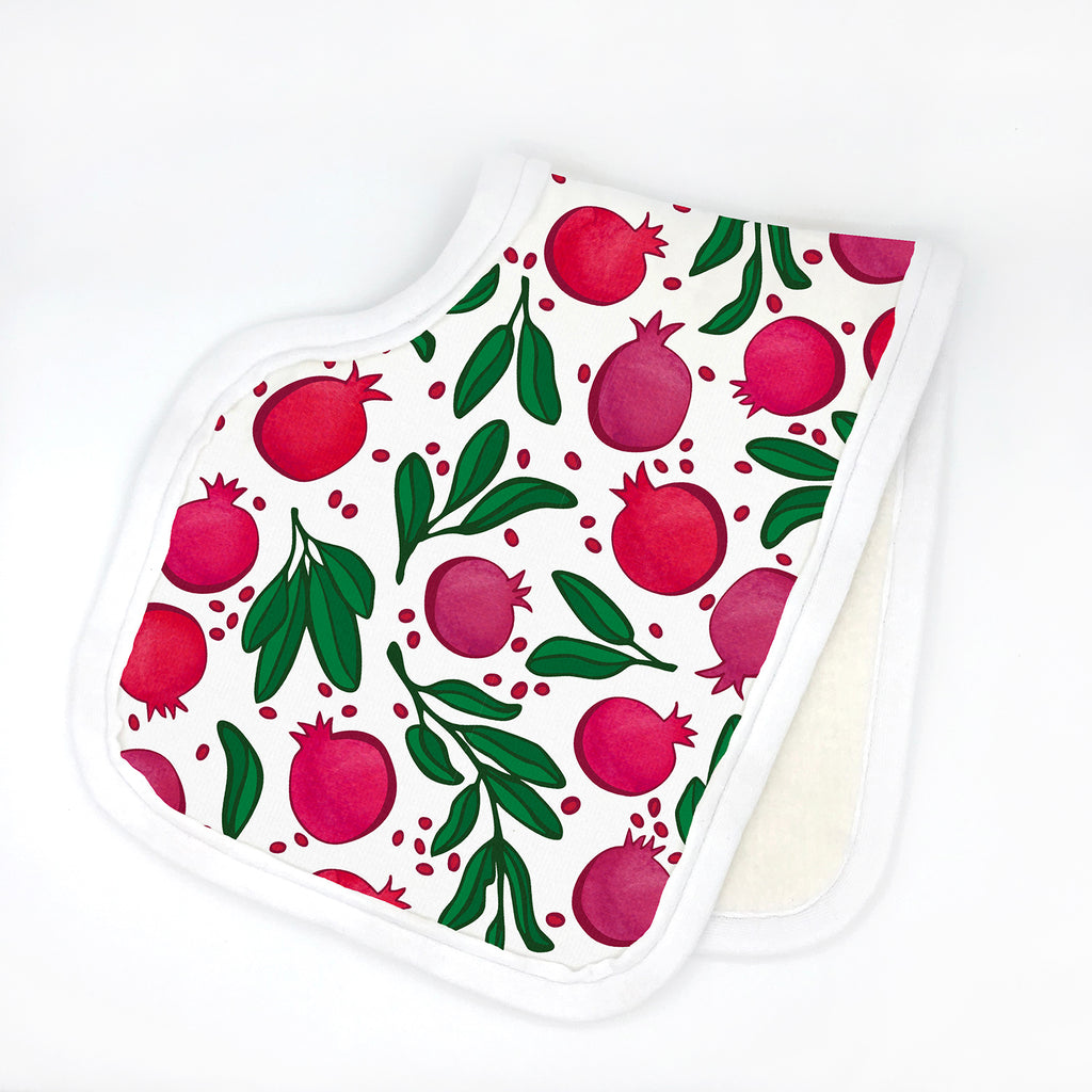 A sweet, handmade organic cotton baby burp cloth with a contoured shape is shown featuring a colorful red, pink purple, green and white Pomegranate fruit print designed by Sunny Day Designs. The burp cloth is shown folded in half with a solid, natural organic cotton fleece on the reverse side and white organic cotton fabric binding around the perimeter of the printed burp cloth.