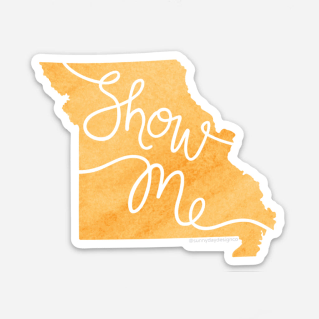 A golden yellow watercolor textured Missouri state-shaped vinyl sticker by Sunny Day Designs is shown on a white background. This fun state-themed sticker features hand lettered text with the Missouri state motto: "Show Me"