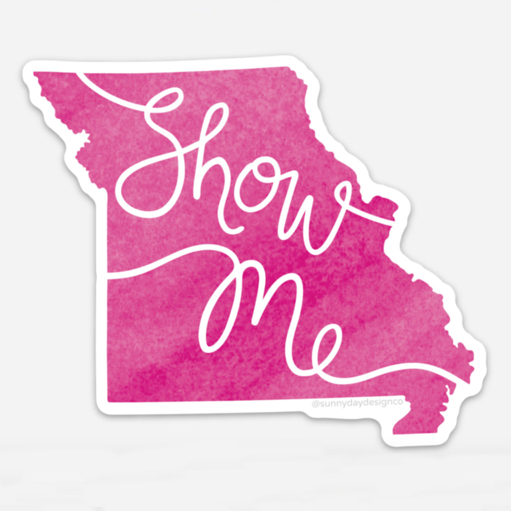 A thin vinyl magnet that is die cut into the shape of the state of Missouri is shown on top of a white background featuring a magenta pink colored watercolor illustration of the state of Missouri with hand lettered text that says "Show Me" within the state shaped design.