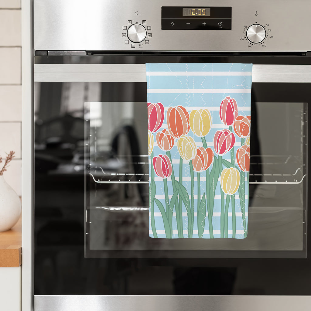 A colorful, Spring tulip printed kitchen towel is shown hanging from the handle of a stainless steel kitchen oven