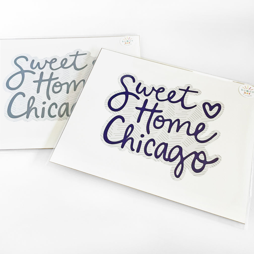 Packaged 8x10 'Sweet Home Chicago' art prints in two color options charcoal gray and navy blue by Sunny Day Designs, featuring handwritten text with a heart accent on a textured background, displayed on a white surface.