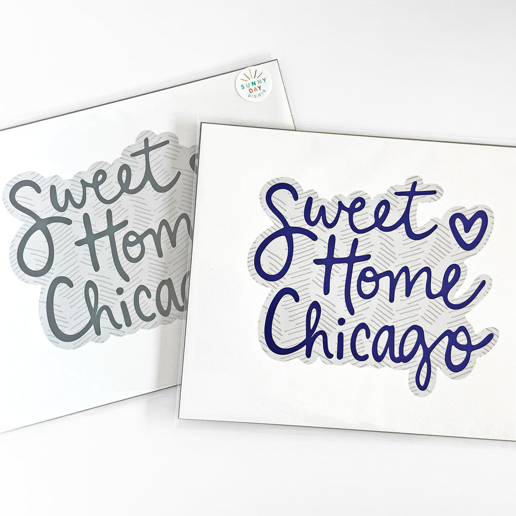 Two 8x10 'Sweet Home Chicago' art prints by Sunny Day Designs, featuring handwritten text in two color options: gray and blue. Each print is packaged and displayed on a white background.
